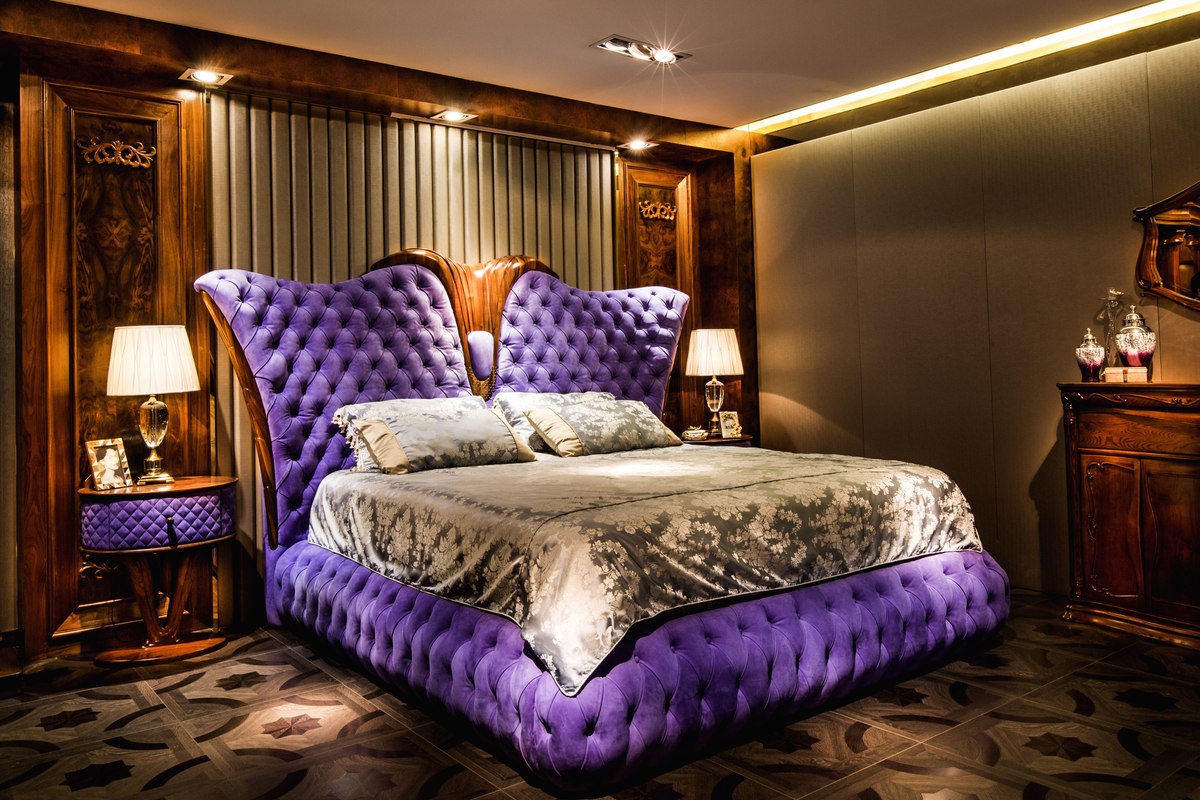 Purple tufted bed with a sculpted timber headboard centre